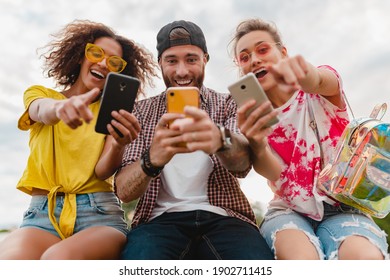 happy young company of smiling friends sitting park using smartphones, man and women having fun together, colorful summer hipster fashion style, communication wireless connecting devices - Powered by Shutterstock