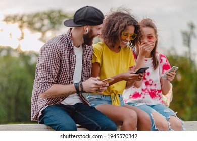 happy young company of smiling friends sitting park using smartphones, man and women having fun together, colorful summer hipster fashion style, communication wireless connecting devices - Powered by Shutterstock