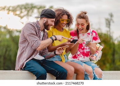 happy young company of smiling friends sitting park using smartphones, man and women having fun together, colorful summer hipster fashion style, communication wireless connecting devices - Powered by Shutterstock