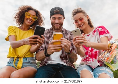 happy young company of smiling friends sitting park using smartphones, man and women having fun together, colorful summer hipster fashion style, communication wireless connecting devices - Powered by Shutterstock