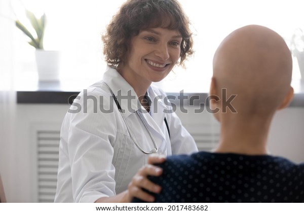 Happy young compassionate kind female oncologist\
doctor supporting bald after chemotherapy patient woman, telling\
effective treatment good news or giving psychological support at\
checkup meeting.