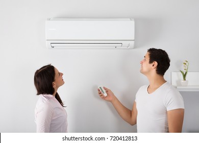 Happy Young Couple Adjusting Temperature Of Air Conditioner By Remote