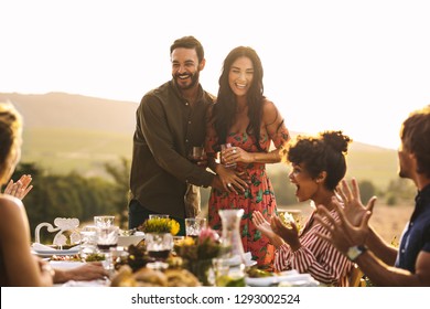 Happy Young Couple Announcing Their Pregnancy At A Party. Man With His Girlfriend Sharing Surprise Pregnancy Announcement With Friends At Dinner Party.