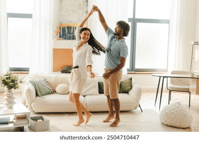 Happy young couple, Asian woman and Indian man dancing at home in their modern living room, having fun. Relationship concept - Powered by Shutterstock