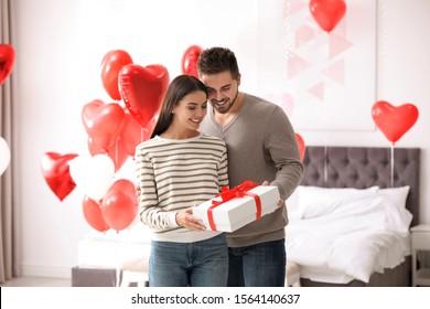 Happy young couple in bedroom decorated with heart shaped balloons. Valentine's day celebration