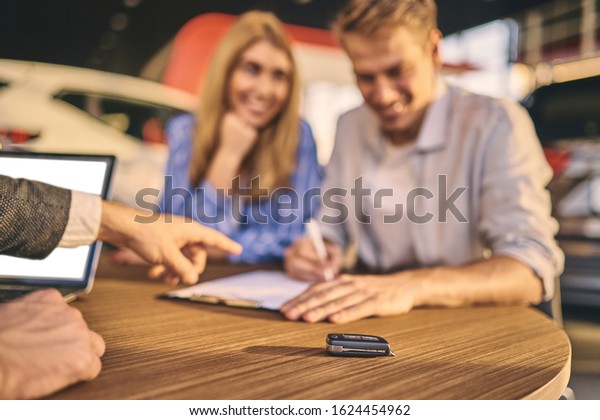 Happy young couple buyers signing a contract of\
buying a new car.