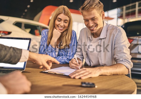 Happy young couple buyers signing a contract of\
buying a new car.