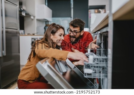 Happy young couple buying dishwasher in store.