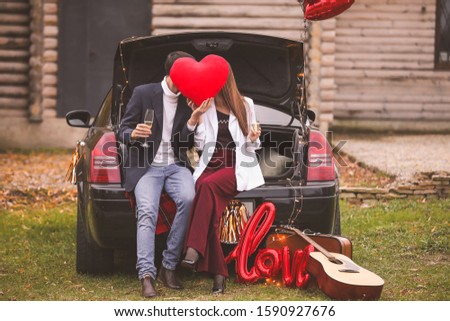 Happy young couple with car and, champagne and heart in park. Valentine's Day celebration