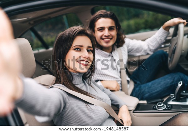 Happy young\
couple in the car, enjoying the trip, taking a selfie for memory,\
good impressions of a modern\
car.