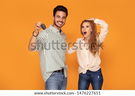 Happy young couple with car key on color background. Boyfriend showing the gift to smiling girlfriend.