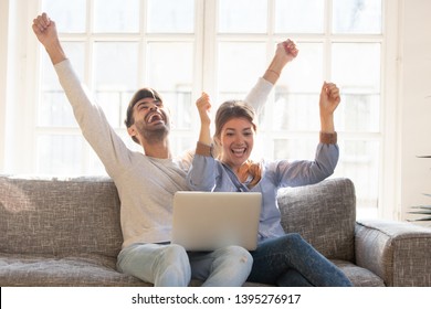 Happy Young Couple Celebrate Online Victory, Screaming With Joy Raising Hands, Looking At Laptop Screen Together, Wife And Husband Receive Good News, Achievement, New Great Offer Opportunity, Success