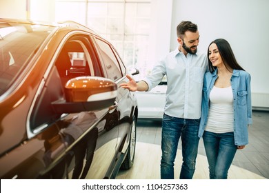 Happy Young Couple Chooses And Buying A New Car For The Family In The Dealership.