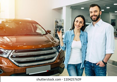 Happy Young Couple Chooses And Buying A New Car For The Family In The Dealership.