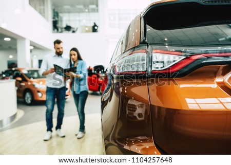 Happy young couple chooses and buying a new car for the family. Visitting the dealership. 
