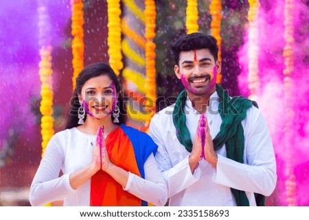 Happy young couple with color on face saying namaste againt flower decorated background - concept of holi festival greeting, wishes and Indian traditional culture
