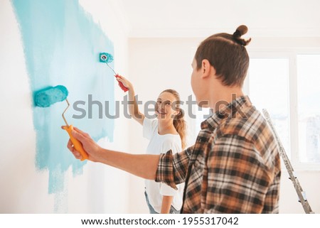 Happy young couple coloring new apartment and paint walls in blue color. 