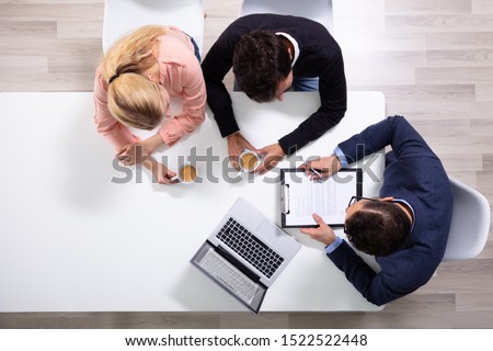 Happy Young Couple Consulting Male Friendly Financial Advisor With Coffee Cups At Office Desk
