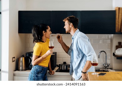 Happy young couple cooking and drinking wine in the kitchen at home together - Powered by Shutterstock