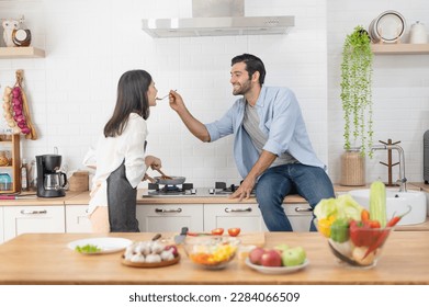 Happy young couple cooking together in the kitchen counter, feeding each other in their kitchen at home - Powered by Shutterstock