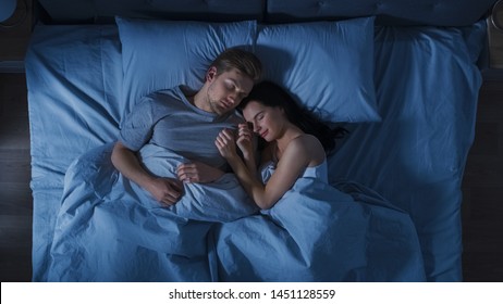 Happy Young Couple Cuddling Together in the Bed Sleeping at Night. Beautiful Girl and Handsome Boy Sleeping Together, Sweetly Embracing Each other. Top Down Shot.