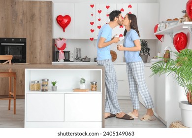 Happy young couple with cups of coffee kissing in kitchen on Valentine's Day - Powered by Shutterstock