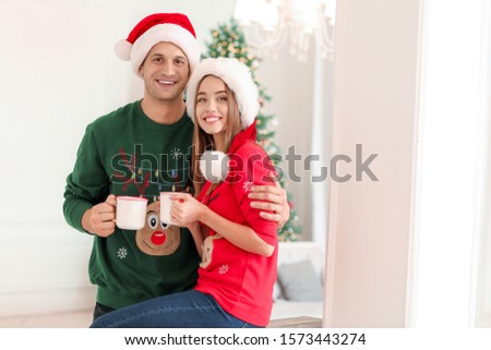 Happy young couple with cups of hot chocolate on Christmas eve at home
