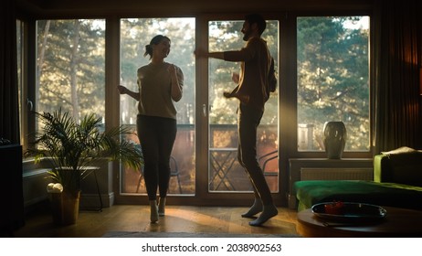 Happy Young Couple Dances In The Living Room. Cheerful Girlfriend And Boyfriend Enjoy True Love, Good Mood And Energetic Music Have Fun At Home. Stylish Interior And Sunny Day