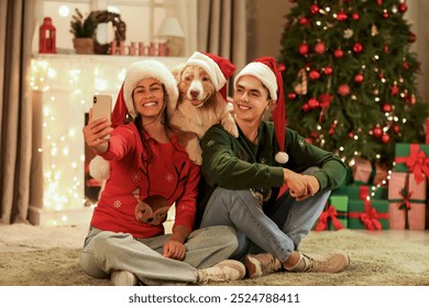 Happy young couple with dog in Santa hats taking selfie at home on Christmas eve - Powered by Shutterstock