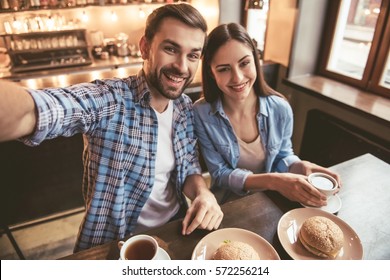 Happy young couple is doing selfie, looking at camera and smiling while sitting at the cafe - Powered by Shutterstock