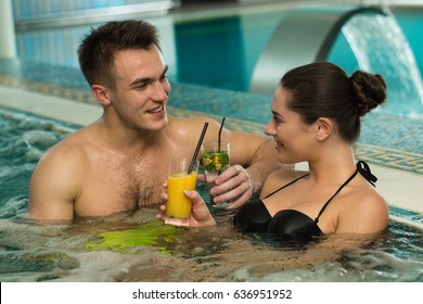 Happy young couple drinking cocktails relaxing in a jacuzzi tub together love relationships couples dating romance vacation travel resort hotel spa treatment relaxation beverages refreshment concept