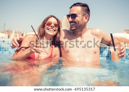 Happy young couple drinking a cocktails in the swimming pool.