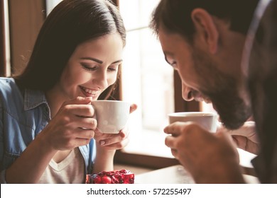 Happy young couple is drinking coffee and smiling while sitting at the cafe