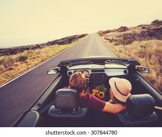 Happy Young Couple Driving Along Country Road in Convertible at Sunset