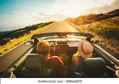 Happy Young Couple Driving Along Country Road in Convertible at Sunset