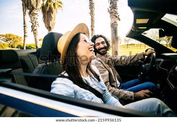 Happy young couple driving cabriolet on\
summer road trip - Cheerful man and woman having fun traveling on\
convertible car - Car rental service\
concept