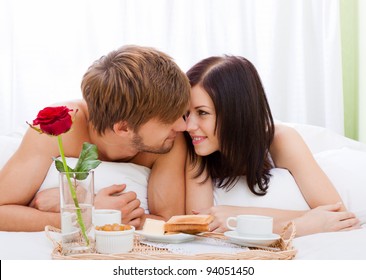 Happy Young Couple Eat Breakfast In Bed In Morning With Red Rose Flower, Lovely Couple Lying In A Bed, Happy Smile Kissing, Concept Of Honeymoon, Valentine Day