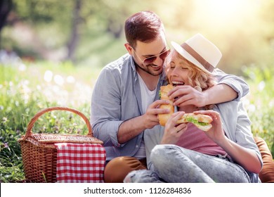 Happy Young Couple Eating Sandwich Outdoors.