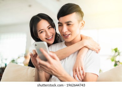  Happy young couple embracing while looking at mobile phone in living room at home
