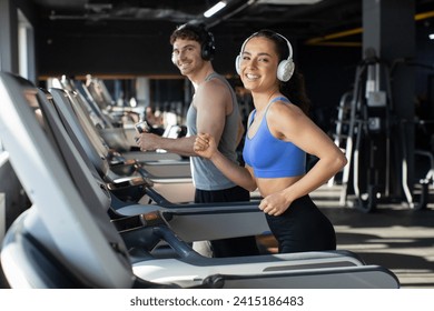 Happy young couple exercising on treadmill and listening music in headphones, enjoying workout in gym and smiling together at camera - Powered by Shutterstock