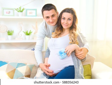 Happy Young Couple family Expecting Baby. Beautiful Pregnant Woman and Her Husband Together Caressing Her Pregnant Belly at Home on a Sofa. Expectant parents, Mom and Dad waiting for their baby.