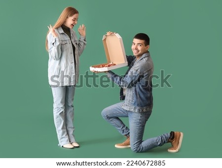 Happy young couple with fresh pizza on green background. Creative marriage proposal