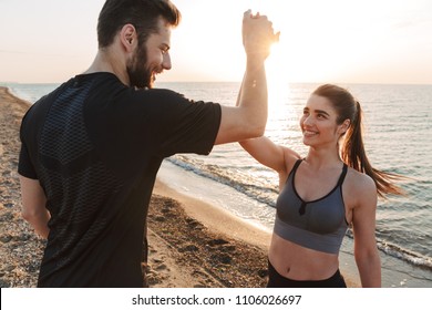 Happy young couple giving high five while standing at the beach - Powered by Shutterstock