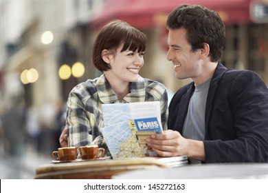 Happy Young Couple With A Guidebook At An Outdoor Cafe