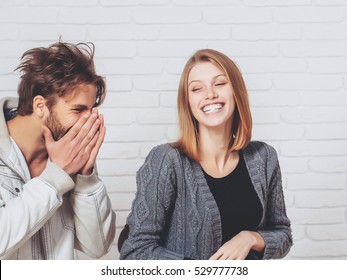 Happy Young Couple Of Handsome Man In Jacket With Pretty Cute Girl Or Beautiful Woman In Knitted Coat Laugh On White Brick Background