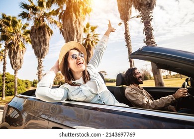 Happy young couple having enjoying summer vacation on convertible car - Man and woman laughing while driving a cabriolet auto outdoors - Travel and holidays concept - Soft focus on woman face - Shutterstock ID 2143697769