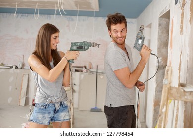 Happy Young Couple Having Fun During Renovation, Playing With Power Drill.