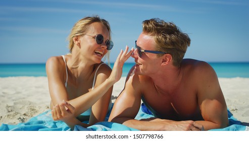 A happy young couple is having fun to apply a sunscreen or sun tanning lotion to take care of their skin during a vacation on a beach. - Powered by Shutterstock