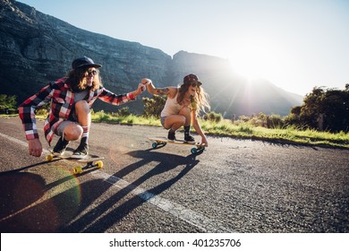 Happy young couple having fun with skateboard on the road. Young man and woman skating together on a sunny day.