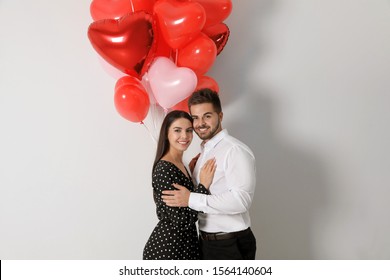 Happy young couple with heart shaped balloons on light background. Valentine's day celebration - Shutterstock ID 1564140604